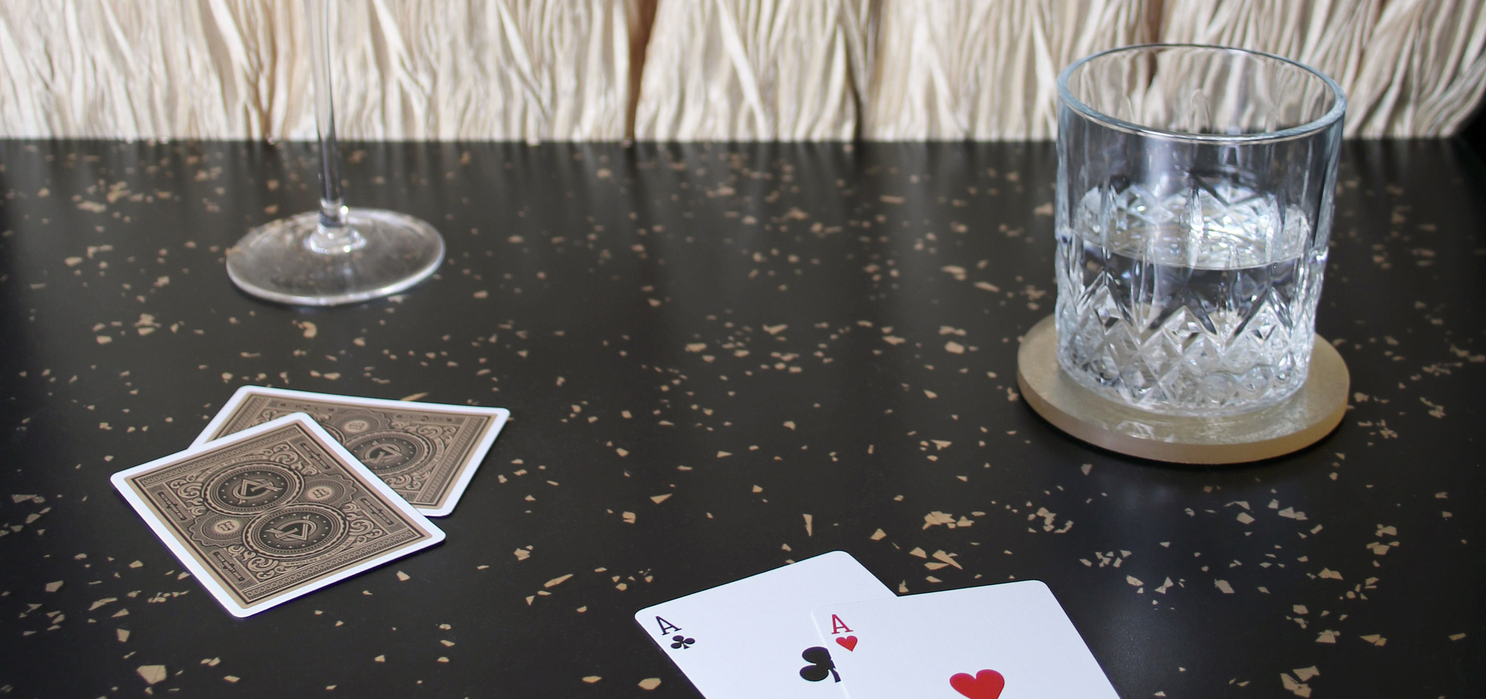 A casino bartop. Two glasses and some cards sit on top of a black countertop embedded with gold flakes.