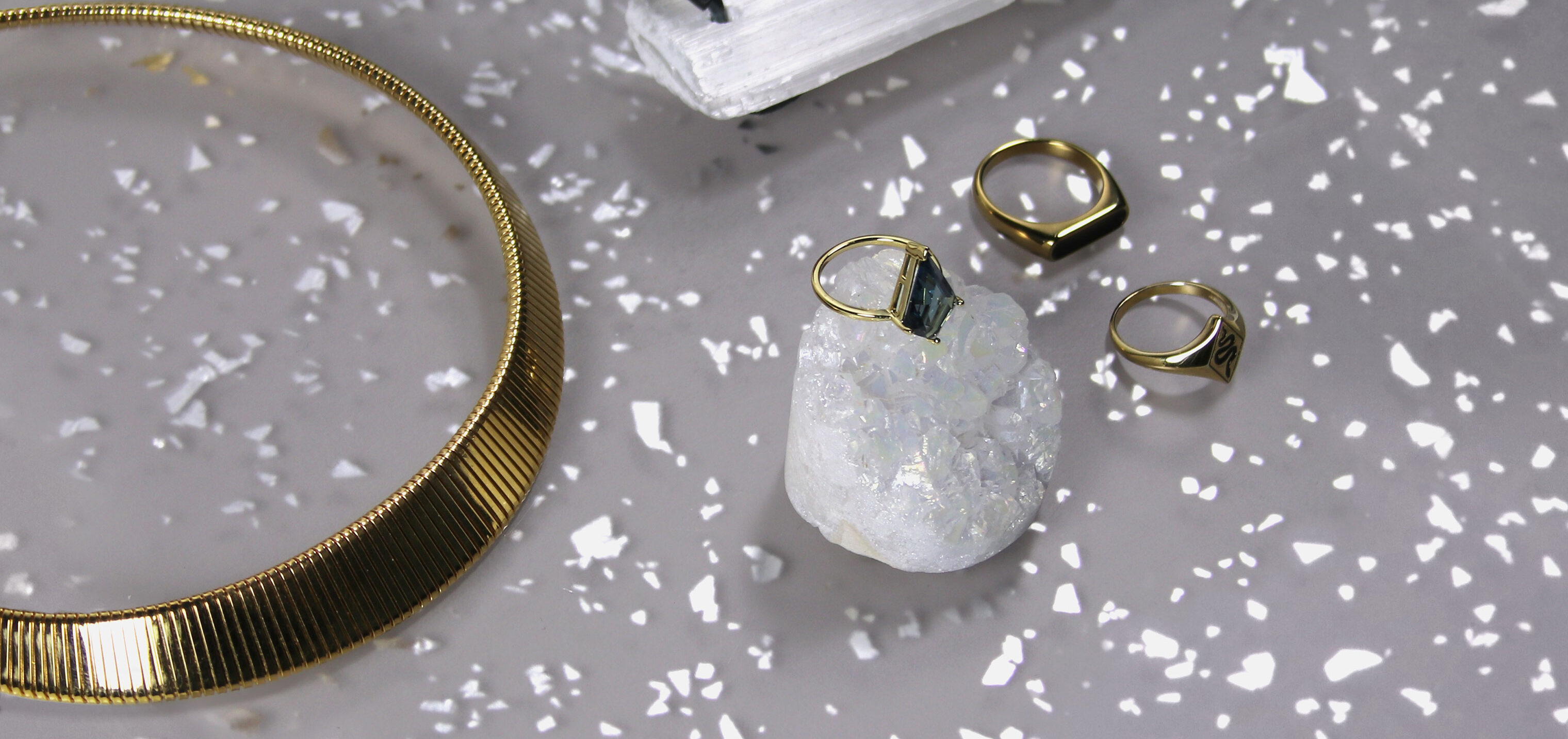 Jewelry items and rock crystals sit on top of a countertop. The countertop is grey with metallic silver flakes.