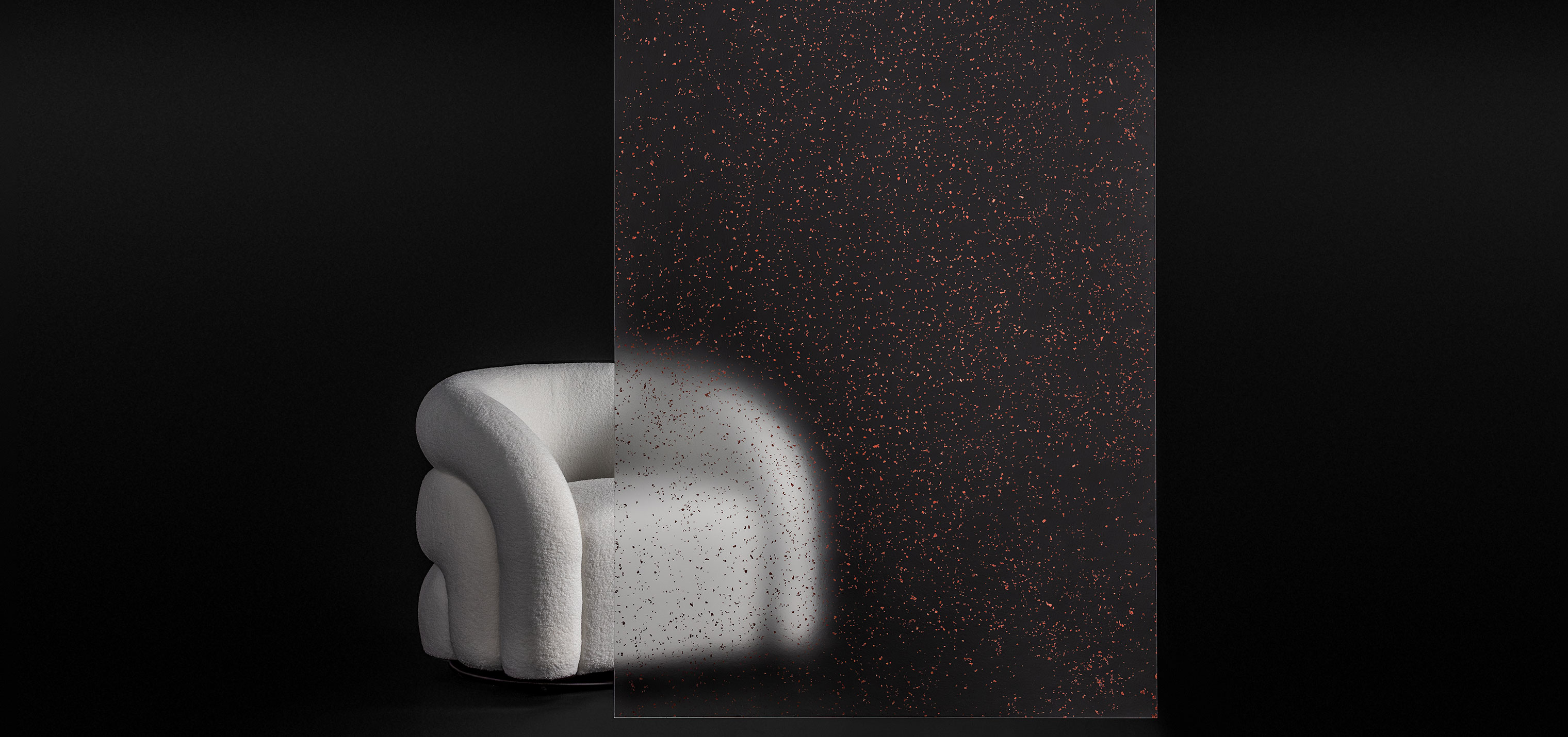 A stuffed white chair sits behind a partition. The partition is clear with red glitter flakes.