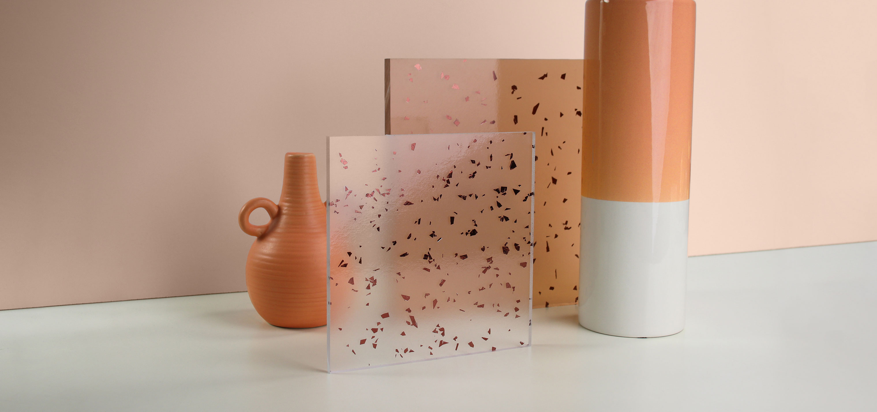 Resin panel material samples and peach-colored vases sit in front of a peach-colored backdrop. One resin panel material sample features red metallic flakes, and the other sample is peach with red metallic flakes.