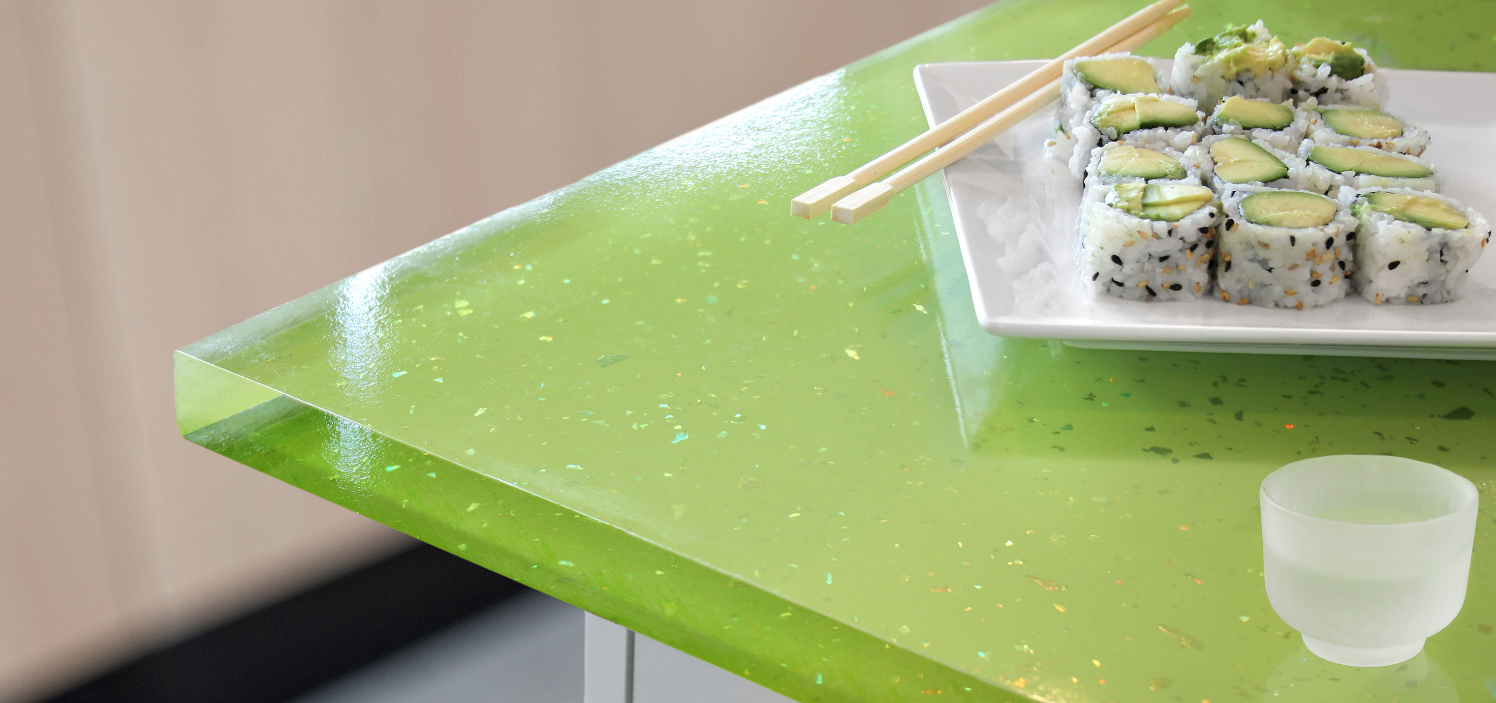 A plate of vegetarian sushi and a cup of sake rest on a bright green, sparkly countertop.